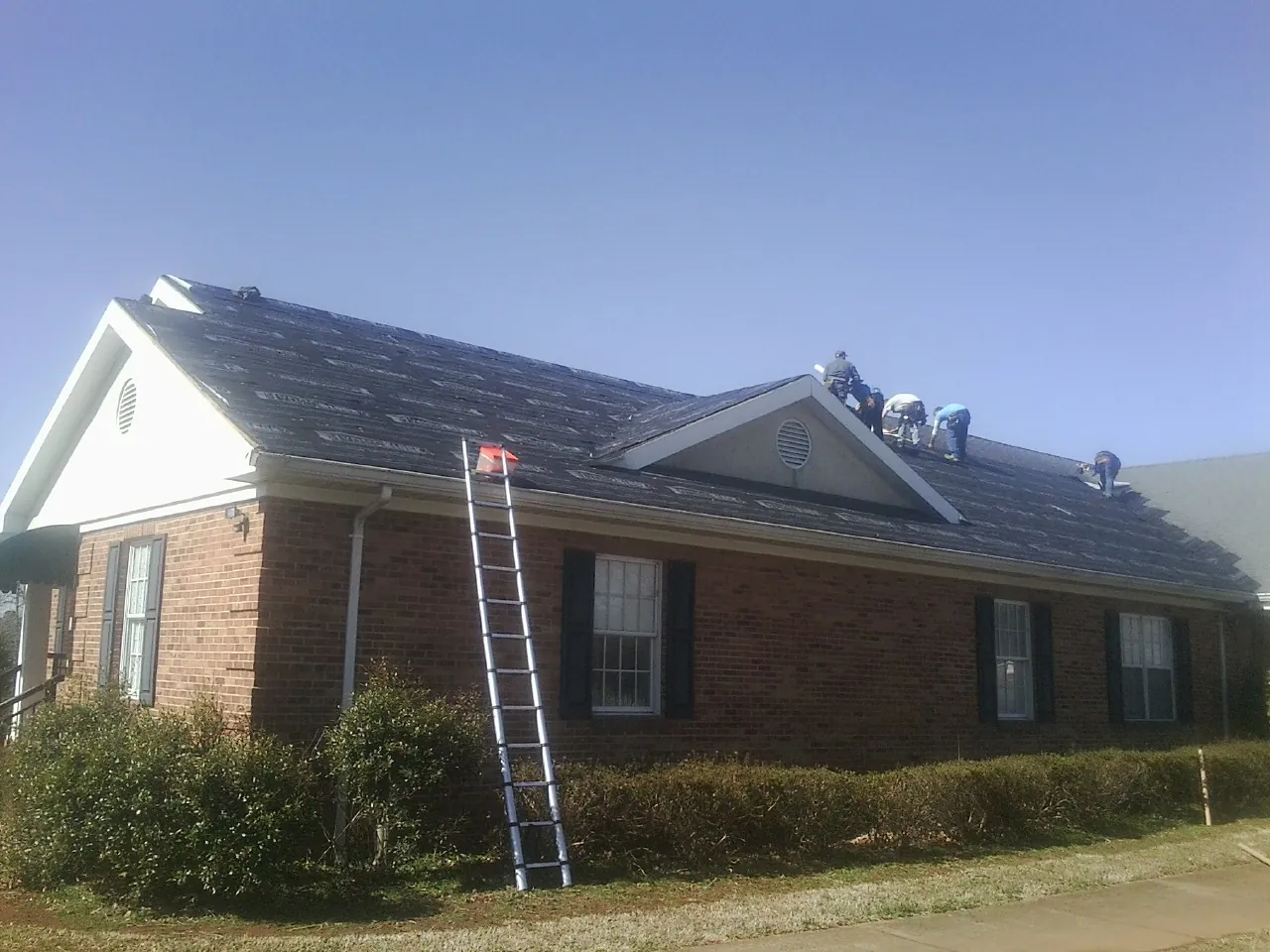 Crew tearing shingles off a brick ranch roof with a ladder set — Emergency Roof Repair work by our crew in Grant Park