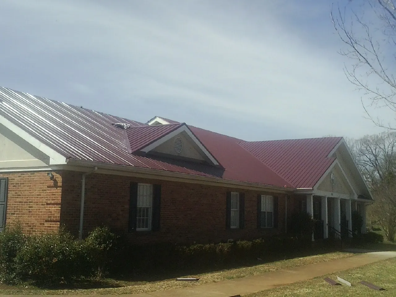 Red metal roof with gabled entries on a long brick building, from a Hail Damage Roof Repair job in Grant Park