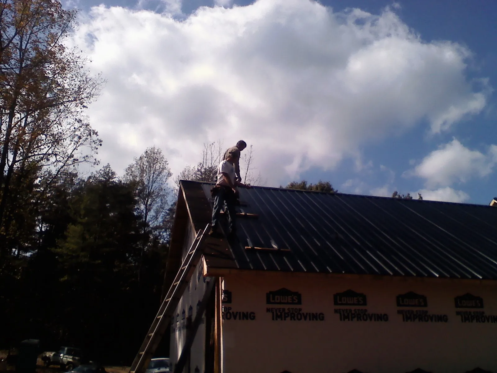 Roofer fastening dark metal panels high against a cloudy sky, from a Roof Inspection job in Grant Park