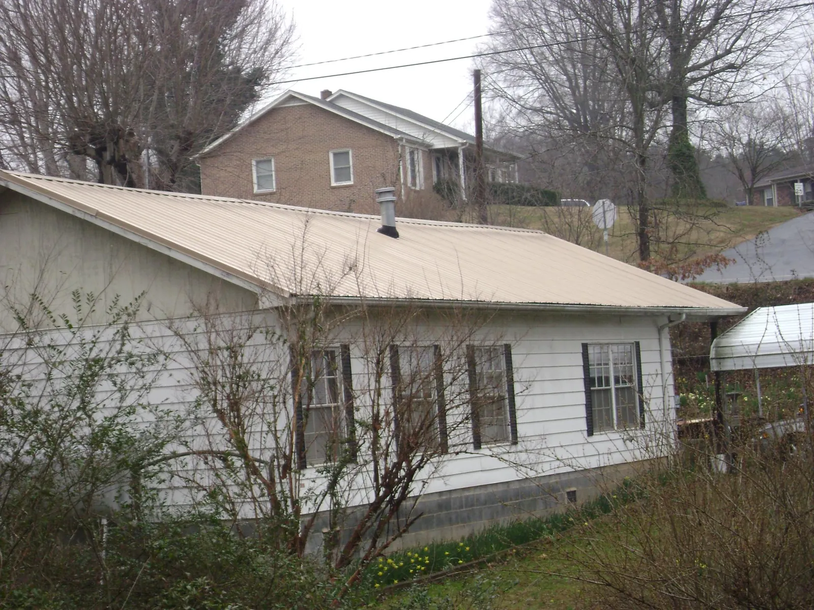 Tan metal roof on a white sided house set into a hillside — Commercial Roofing by Roofing Brothers in Grant Park